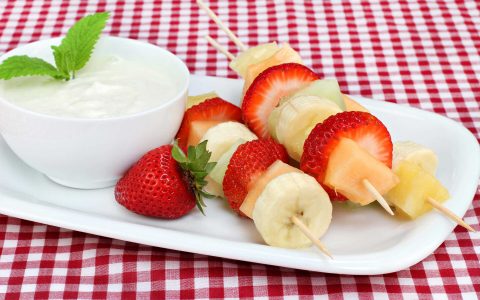 brochettes de fruits sur une assiette blanche près d'un bol de yogourt