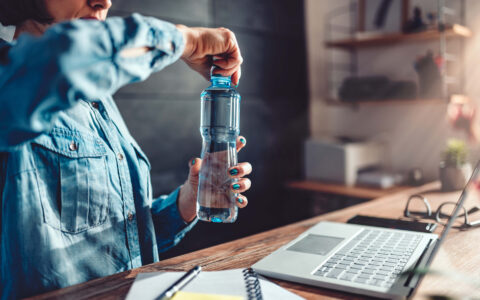 femme ouvrant sa gourde d'eau devant bureau