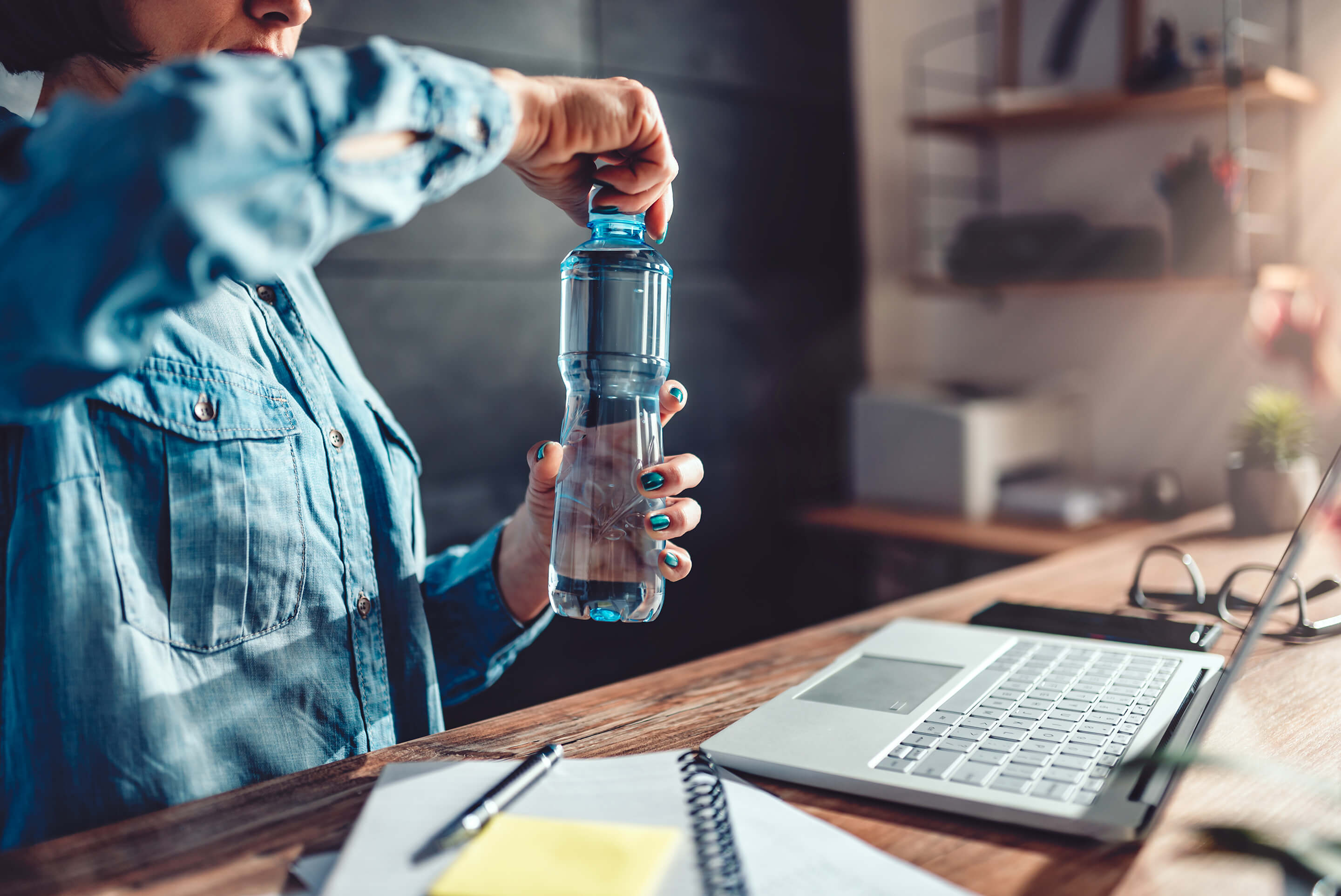 femme ouvrant sa gourde d'eau devant bureau