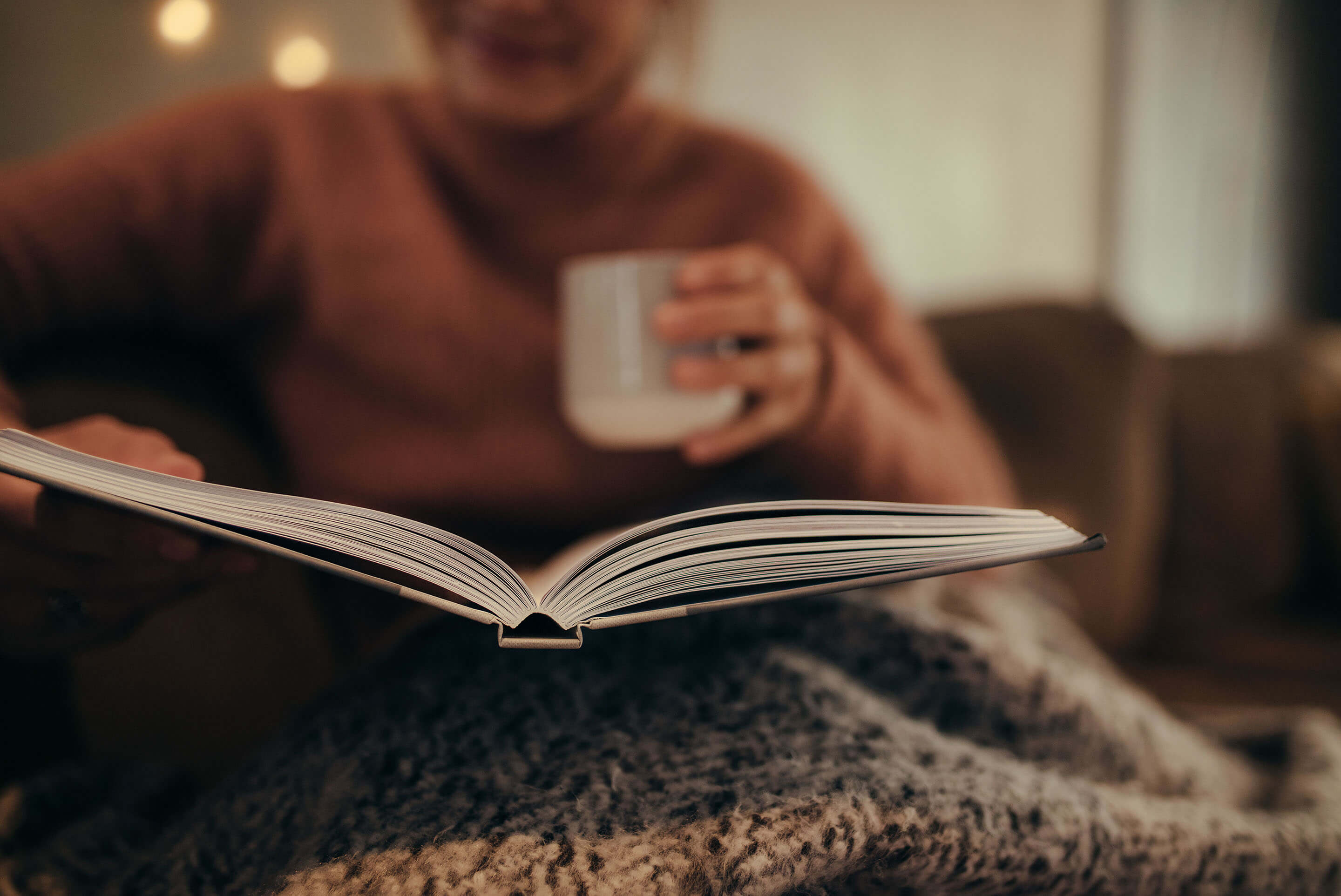 femme lisant un livre en buvant une boisson chaude